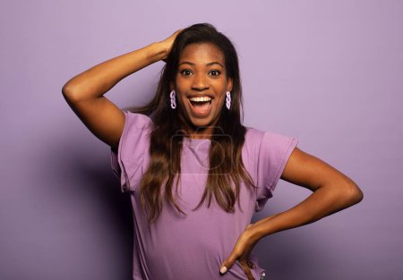 Photo for Young afro american woman is amazed with her mouth open, looks away in surprise. Portrait over purple background. - Royalty Free Image
