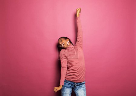 Photo for Cheerful and beautiful young dark-skinned woman in a pink sweater dancing and laughing on a pink background - Royalty Free Image