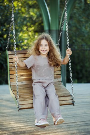 Foto de Alegre niña de seis años monta en un columpio en un parque de verano, estilo de vida y el concepto de la gente. - Imagen libre de derechos
