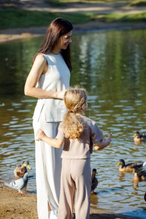 Téléchargez les photos : Maman et petite fille donnent des miettes de pain aux canards et goélands près du lac - en image libre de droit