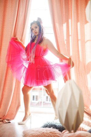 Photo for Young happy woman with dreadlocks hairstyle wearing pink dress, doll style, bright make, up in the pink room. - Royalty Free Image
