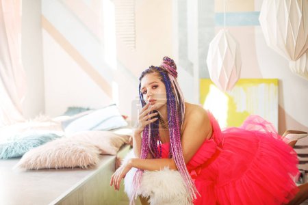 Foto de Mujer feliz joven con rastas peinado con vestido rosa, estilo muñeca, maquillaje brillante, hasta en la habitación rosa. - Imagen libre de derechos