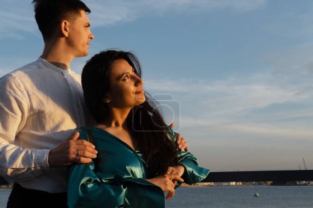 Téléchargez les photos : Un jeune couple amoureux de nationalités différentes admire le coucher de soleil près de l'eau sur le remblai. - en image libre de droit