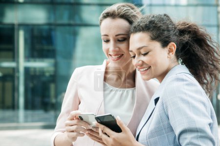 Foto de Negocios, gente, tehnología y concepto de éxito: Dos mujeres de negocios con teléfono móvil cerca de la oficina - Imagen libre de derechos