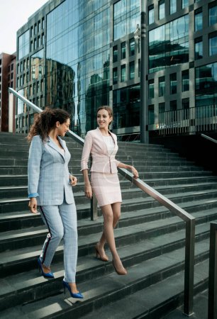Foto de Concepto de negocio, gente y estilo de vida: dos empleados de oficina juntos en escaleras cerca del moderno edificio de negocios. - Imagen libre de derechos