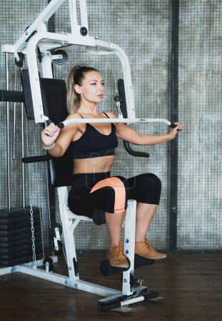 Foto de Mujer joven deportiva haciendo ejercicio en la estación múltiple en el gimnasio para los músculos del brazo y los hombros. Ejercicio de fitness en gimnasio. - Imagen libre de derechos