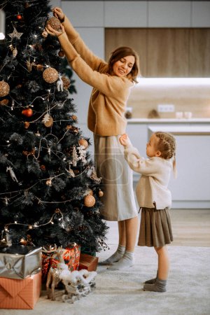Foto de Familia, vacaciones de invierno y concepto de personas. Feliz joven madre e hija pequeña decorando el árbol de Navidad en casa. - Imagen libre de derechos