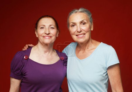 Téléchargez les photos : Deux jolies amies âgées sur fond rouge. Concept de style de vie. - en image libre de droit