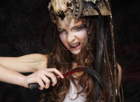 Téléchargez les photos : Jeune femme au maquillage agressif tenant une faucille. Halloween. Fête costumée. - en image libre de droit