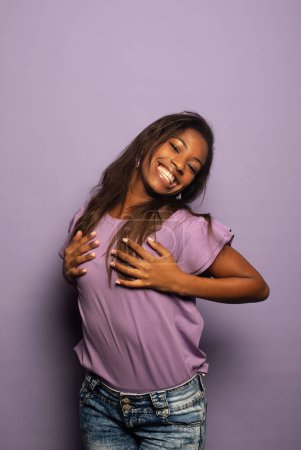 Foto de Encantadora mujer afroamericana con camisa morada sonríe felizmente. Retrato sobre fondo lila - Imagen libre de derechos