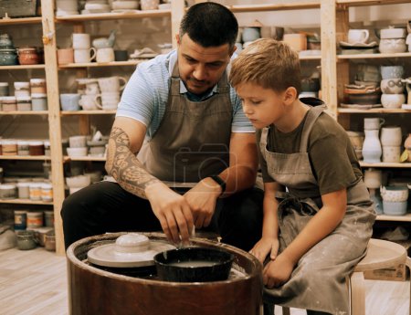 Téléchargez les photos : Un bel homme confiant et un petit garçon fabriquant du pot en céramique dans la classe de poterie. Fils et père sont créatifs ensemble. - en image libre de droit