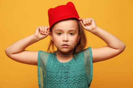 Photo for Stylish little girl model in a red hat and blue dress on a yellow background. Fashion and people concept. - Royalty Free Image