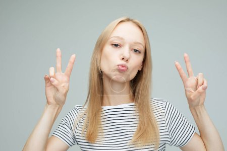 Photo for Portrait of a pretty young blond woman showing the peace sign on grey color background - Royalty Free Image