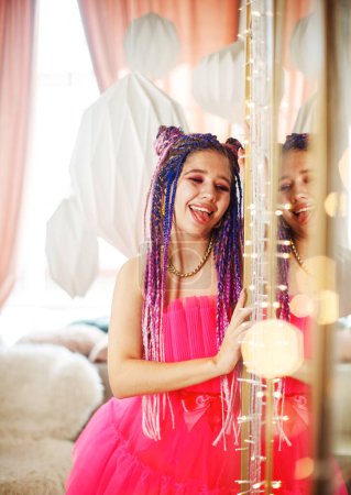 Foto de Joven bonita mujer con rastas peinado usando vestido rosa, estilo muñeca, maquillaje brillante, hasta en la habitación rosa. - Imagen libre de derechos