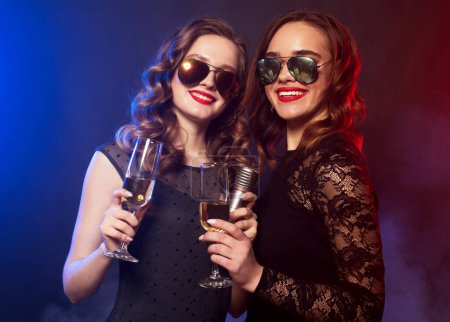 Foto de Dos alegres y encantadoras jóvenes amigas con bolas de discoteca bebiendo champán y divirtiéndose juntas - Imagen libre de derechos