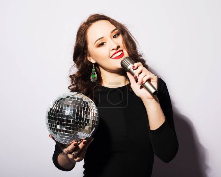 Téléchargez les photos : Style de vie, fête et concept de personnes : jeune belle femme dans une robe de cocktail tenant un microphone et une balle disco. - en image libre de droit