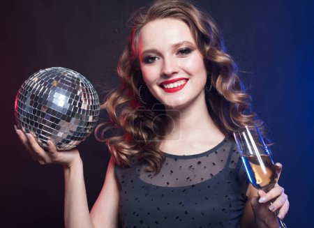 Foto de Joven mujer rubia de lujo con vestido brillante sosteniendo bolas de discoteca y una copa de champán. Tiempo de fiesta. - Imagen libre de derechos