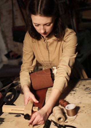Foto de Joven morena mujer trabaja en un taller, cose bolsas de cuero - Imagen libre de derechos