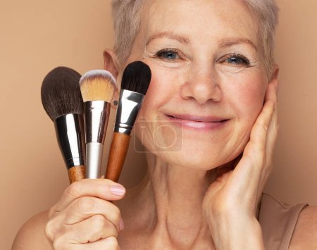 Photo for An elderly woman with short hair holds cosmetic brushes, mature beauty at any age. - Royalty Free Image