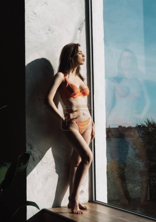Photo for Young beautiful woman with long hair in lace lingerie near big window. Summer sunny day. - Royalty Free Image