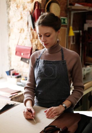 Photo for Young brunette woman works in a workshop, sews leather bags - Royalty Free Image