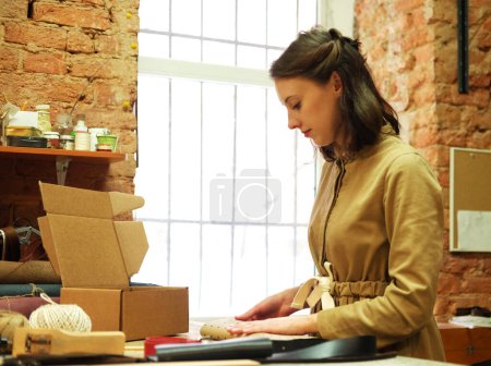 Photo for Young woman folds packing box in sewing workshop - Royalty Free Image