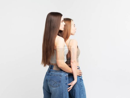 Téléchargez les photos : Deux jeunes femmes amies aux cheveux longs isolées sur fond gris blanc - en image libre de droit