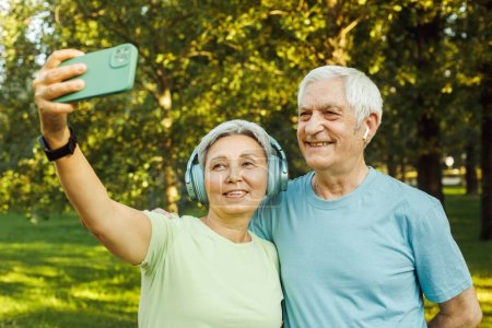 Photo for Technology, relationship and old people concept - lovely senior couple with smartphone taking selfie and hugging at park - Royalty Free Image