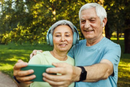 Téléchargez les photos : Heureux couple de personnes âgées prenant selfie assis dans le parc à l'extérieur. Aimez la convivialité et le concept acive de vitalité des aînés - en image libre de droit
