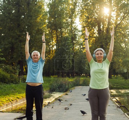 Téléchargez les photos : Yoga au parc. Couple de personnes âgées faisant de l'exercice à l'extérieur. Heure d "été. - en image libre de droit