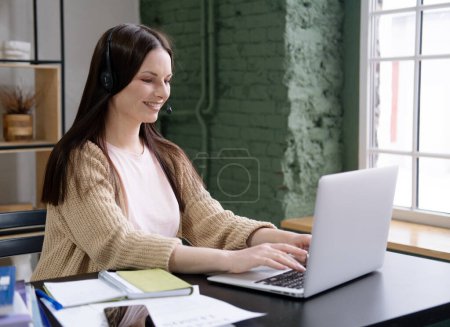 Foto de Joven mujer alegre con el pelo largo trabaja en un portátil moderno en su oficina en casa. - Imagen libre de derechos