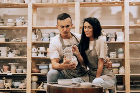 Téléchargez les photos : Un jeune couple souriant travaille dans un atelier de poterie. Peindre un vase. Le concept de passe-temps, mode de vie et relations. - en image libre de droit