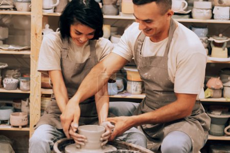 Téléchargez les photos : Jeune couple amoureux travaillant ensemble sur une roue de potier dans un atelier d'artisanat. Style de vie et concept de passe-temps. - en image libre de droit
