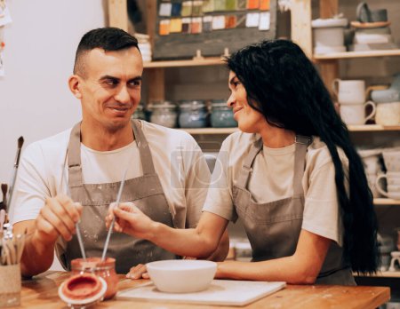 Téléchargez les photos : Un jeune couple souriant travaille dans un atelier de poterie. Peindre un vase. Le concept de passe-temps, mode de vie et relations. - en image libre de droit