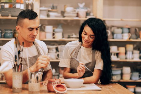 Foto de Una joven pareja sonriente trabaja en un taller de cerámica. Pintando un jarrón. El concepto de aficiones, estilo de vida y relaciones. - Imagen libre de derechos