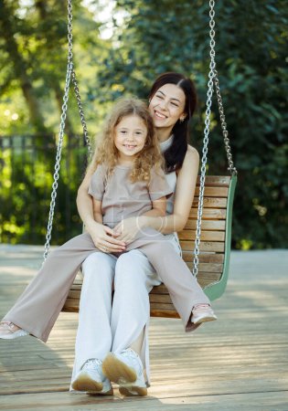 Photo for Young Mom and 7s daughter swing on a swing. Caucasian woman and little girl have fun on the playground. - Royalty Free Image