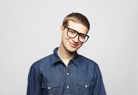 Téléchargez les photos : Jeune bel homme porter des lunettes de vue en regardant la caméra sur fond gris - en image libre de droit