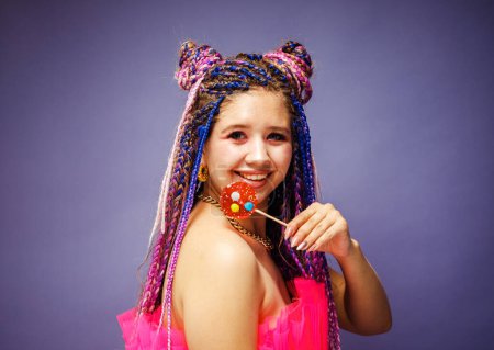 Foto de Joven mujer sonriente con peinado dreadlocks y maquillaje creativo en estilo muñeca con dulces sobre fondo púrpura - Imagen libre de derechos