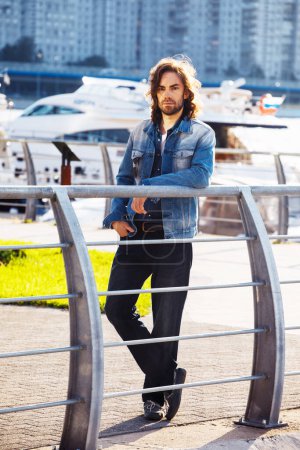 Photo for Stylish handsome male model with long hair posing near river on a summer day. Fashion and lifestyle concept. - Royalty Free Image