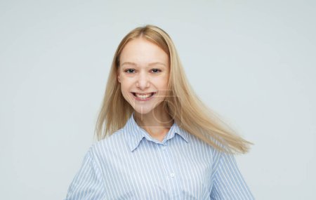 Foto de Encantadora mujer joven con el pelo rubio con camisa azul sonriendo aislado sobre fondo de color gris claro - Imagen libre de derechos