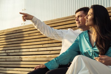 Una pareja de jóvenes amantes de diferentes nacionalidades se sienta en un banco y admira la puesta de sol. Familia joven.