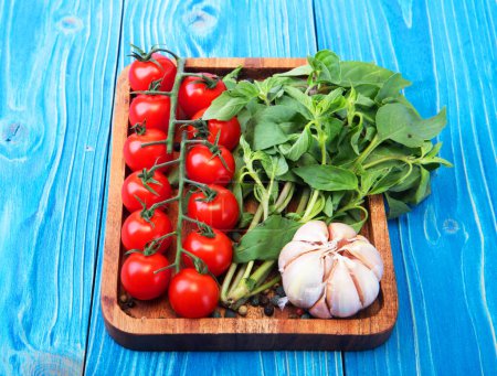 Foto de Tomates, perejil y ajo en una bandeja, sobre una mesa de madera azul. De cerca.. - Imagen libre de derechos