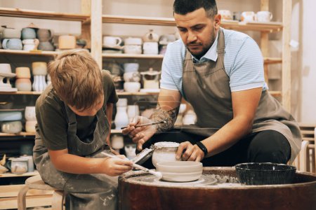 Photo for Confident young man and little boy making ceramic pot on the pottery class. Lifestyle and people concept. - Royalty Free Image