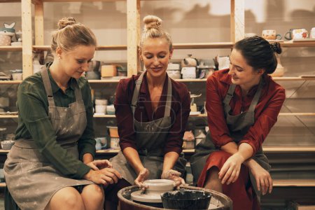Photo for A company of three pretty young women friends make ceramic mugs in a pottery workshop. Lifestyle and people concept. - Royalty Free Image