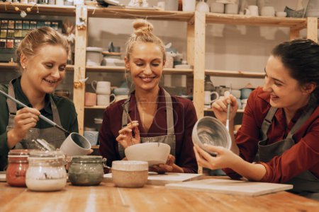 Photo for A company of three cheerful young women friends are painting ceramics in a pottery workshop. Lifestyle and people concept. - Royalty Free Image