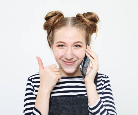 Photo for Young smiling blond woman with buns hair hearing exciting news on smartphone over white background - Royalty Free Image