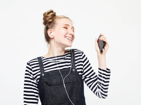 Young smiling woman with buns hair listening to the music with smartphone.
