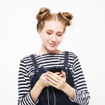 Young smiling woman with buns hair listening to the music with smartphone.