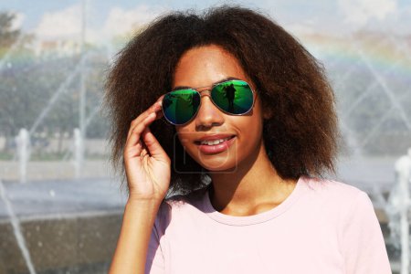 Photo for Pretty woman wearing sunglasses with perfect teeth and dark clean skin having rest outdoors - Royalty Free Image