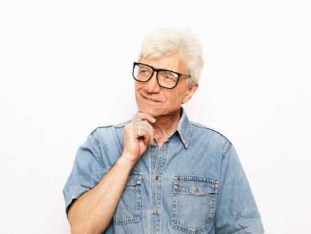 Photo for Old age, problem and people concept: Portrait of thoughtful old man wearing denim shirt and glasses over white background - Royalty Free Image